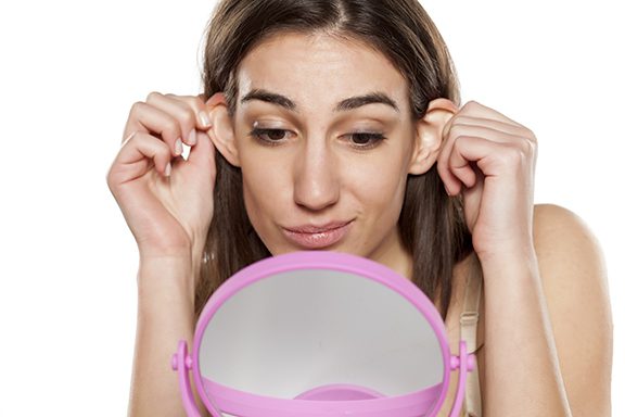 photo of a beautiful young woman looks at her ears in front of the mirror